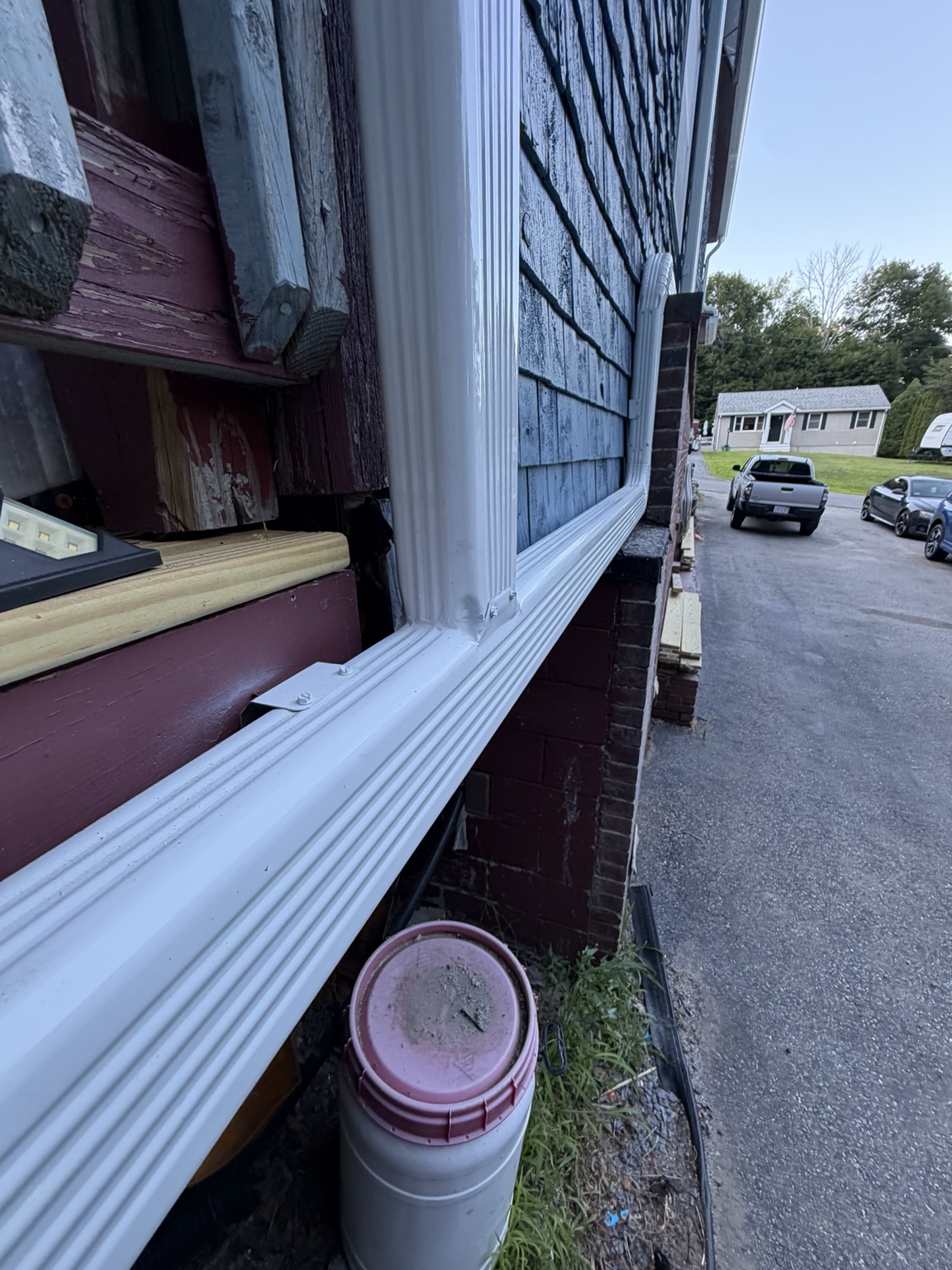 Six-inch high gloss white seamless gutter system with joining downspouts routing roof water to the back of the home